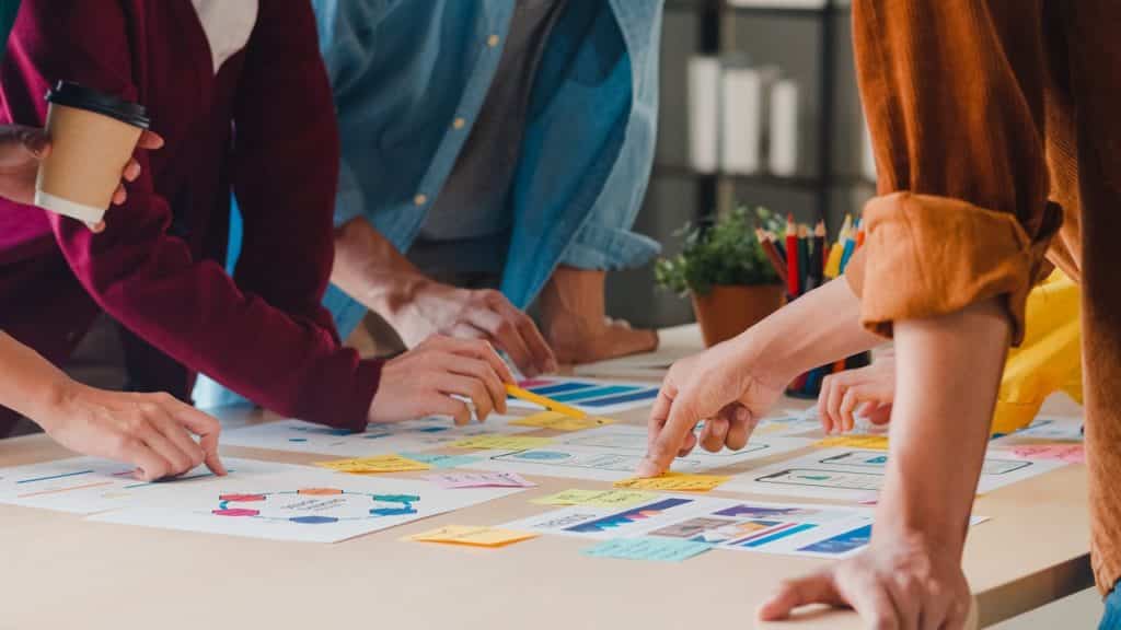 reunião com varias pessoas observando papéis com gráficos e post its com anotações