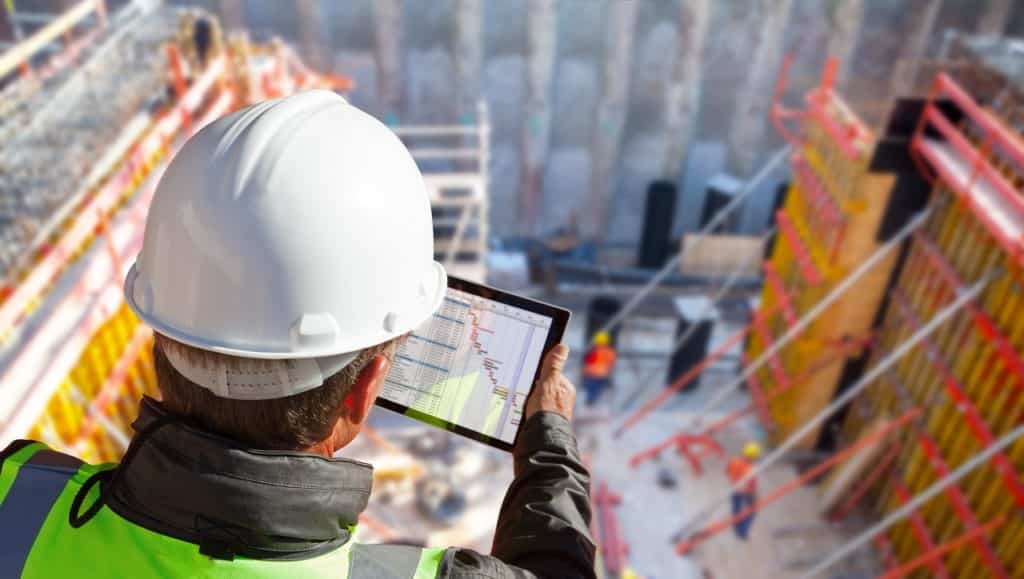 engenheiro olhando dados em um tablete observando o canteiro de obras de cima