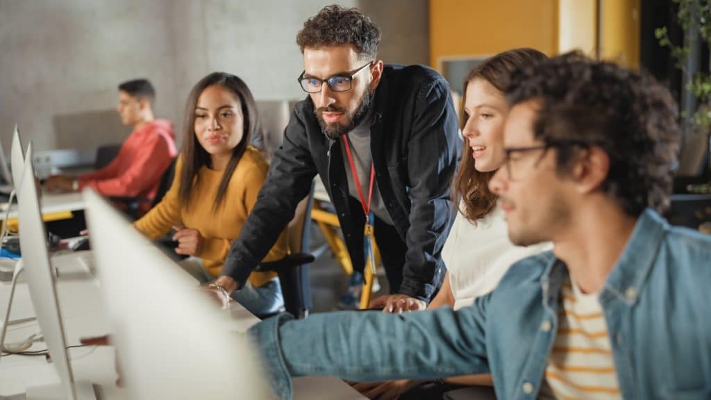 4 pessoas em reunião observando a tela de um computador