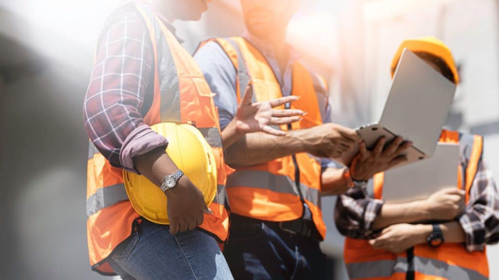 tres trabalhadores da construção civil olhando um notebook